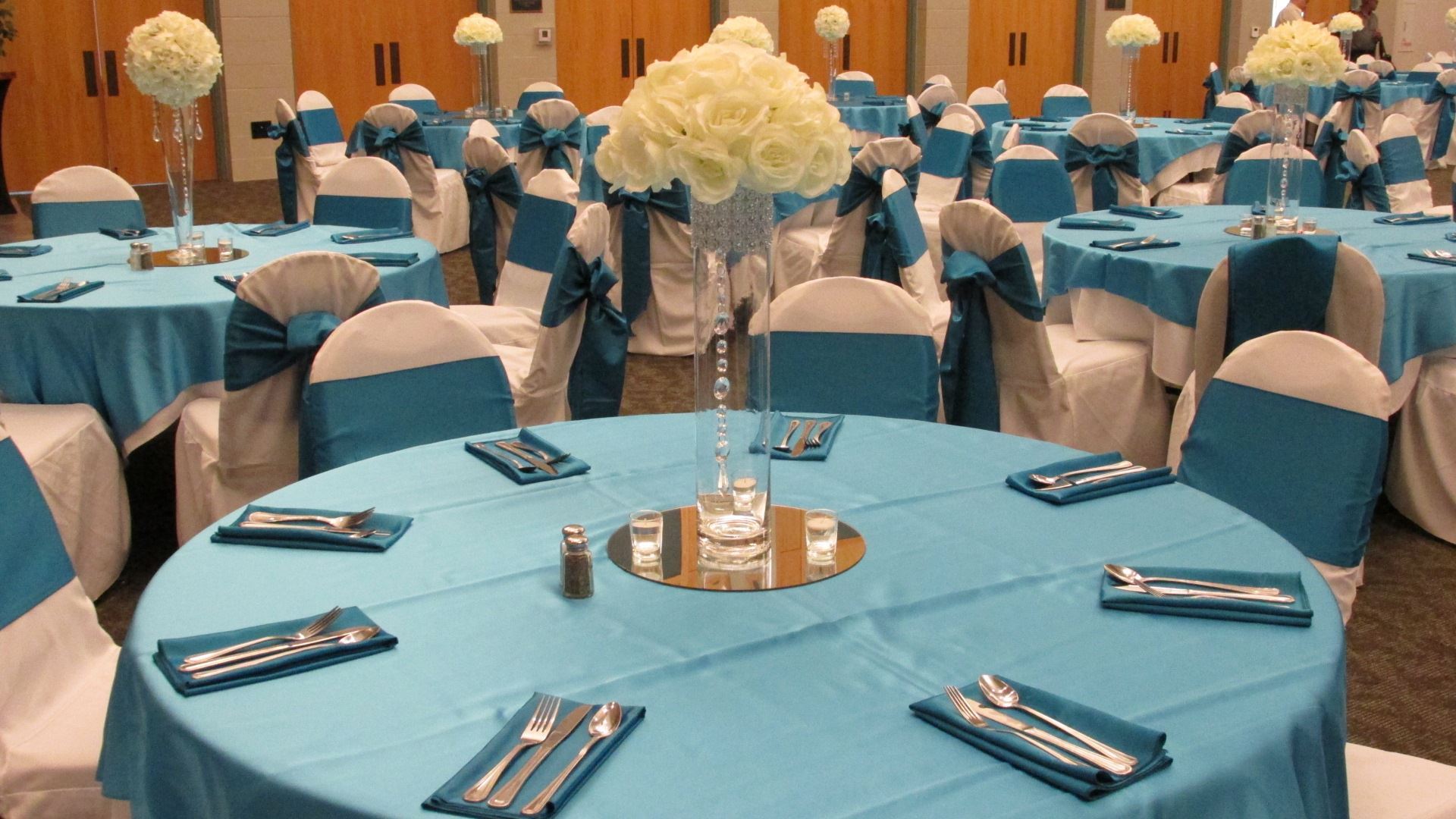 Turquoise and white wedding reception close up of a table setting with white rose center pieces